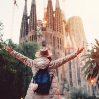 Rear view of young woman in front of Sagrada Familia with arms outstretched enjoying the beautiful city